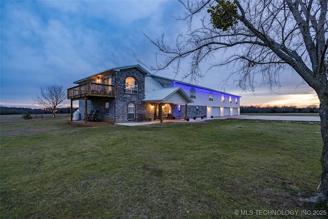1522 Burney Cemetary, Calera, OK 74730 - back of property at dusk with an attached garage, stone siding, a balcony, driveway, and a yard