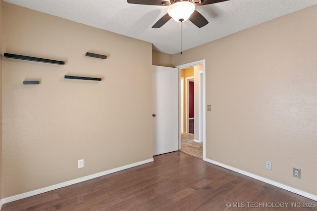 empty room with a textured ceiling, a ceiling fan, dark wood-type flooring, and baseboards