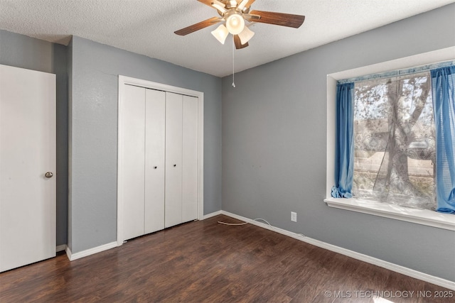 unfurnished bedroom with dark wood-style floors, a textured ceiling, baseboards, and a closet