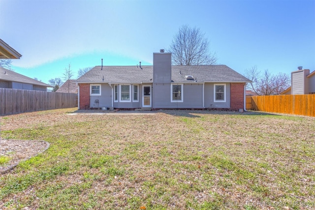 rear view of house with a yard, a fenced backyard, brick siding, and a chimney