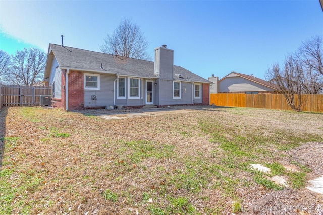 back of house with brick siding, fence, central AC unit, a chimney, and a yard