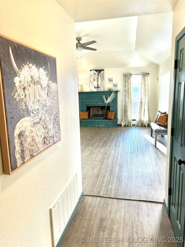 interior space with vaulted ceiling, wood finished floors, ceiling fan, a fireplace, and visible vents