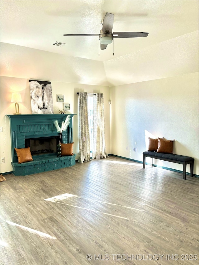 living room featuring visible vents, wood finished floors, baseboards, a brick fireplace, and ceiling fan