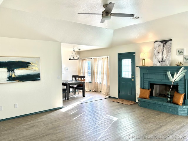 living room with visible vents, a textured ceiling, a brick fireplace, and wood finished floors