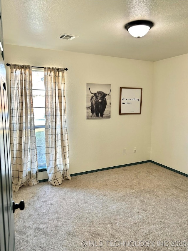 spare room featuring baseboards, carpet, visible vents, and a textured ceiling