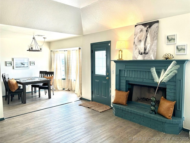 foyer featuring a brick fireplace, baseboards, wood finished floors, a notable chandelier, and a textured ceiling