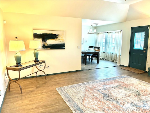 foyer featuring an inviting chandelier, vaulted ceiling, wood finished floors, and baseboards