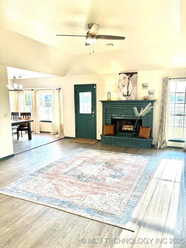 living area with a brick fireplace, wood finished floors, visible vents, and ceiling fan with notable chandelier