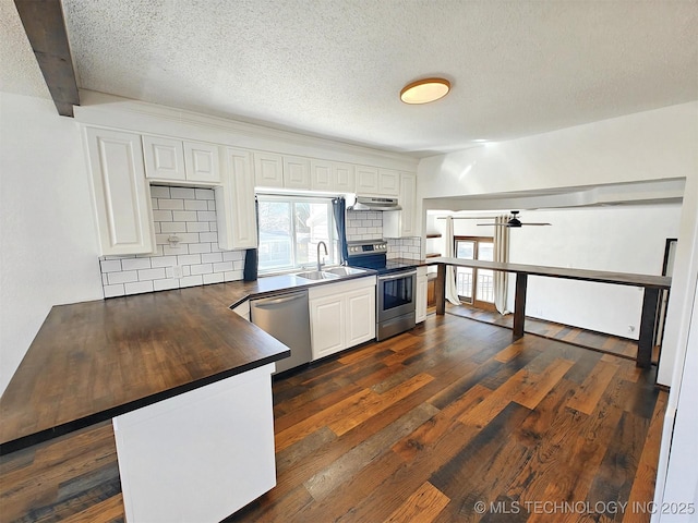 kitchen with dark wood-type flooring, under cabinet range hood, dark countertops, stainless steel appliances, and decorative backsplash