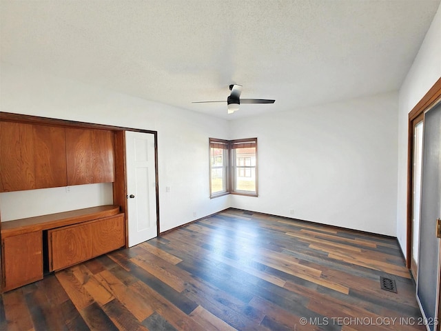 unfurnished bedroom featuring ceiling fan, dark wood-type flooring, visible vents, and a textured ceiling