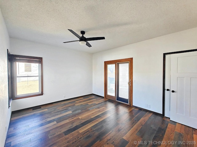 unfurnished room with a wealth of natural light, a textured ceiling, and dark wood finished floors