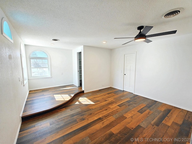 empty room with hardwood / wood-style floors, baseboards, visible vents, and a textured ceiling