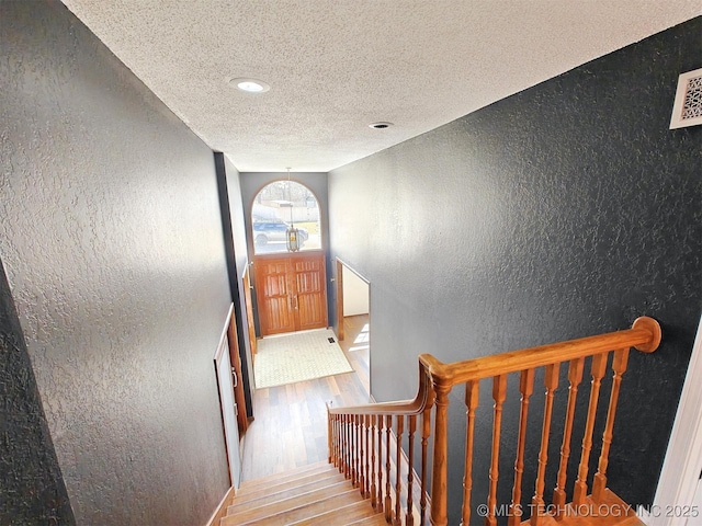 stairway featuring wood finished floors, a textured wall, visible vents, and a textured ceiling