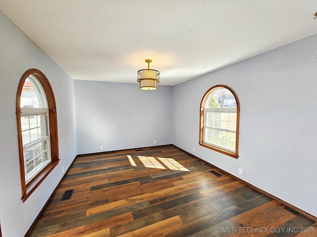 empty room featuring dark wood-style floors, visible vents, and a textured ceiling