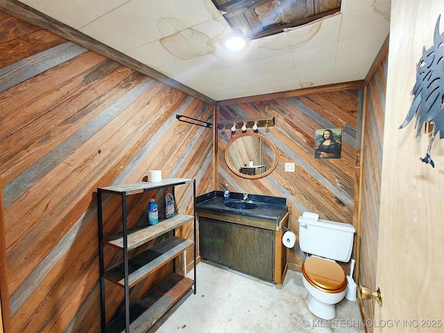 bathroom with concrete floors, wood walls, toilet, and vanity