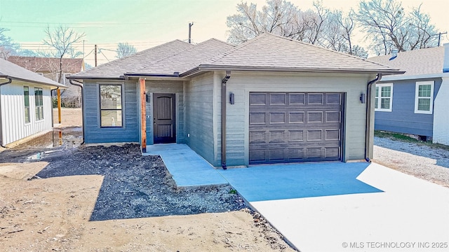 single story home featuring concrete driveway, an attached garage, and a shingled roof