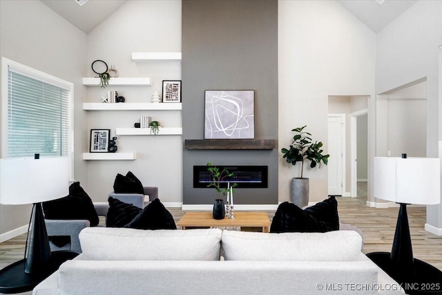 living room featuring baseboards, wood finished floors, high vaulted ceiling, and a glass covered fireplace