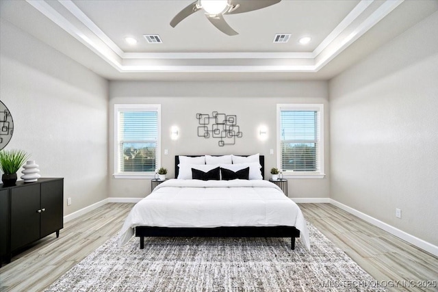 bedroom with a tray ceiling, visible vents, and light wood-type flooring