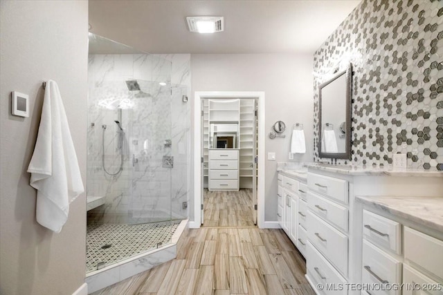 bathroom with wood finish floors, visible vents, a marble finish shower, vanity, and a spacious closet