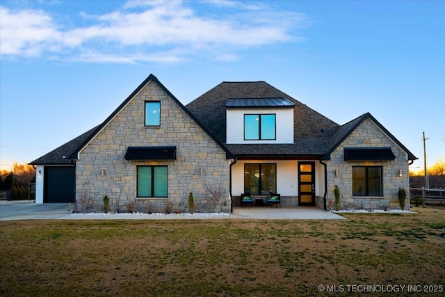 back of house with stone siding, a lawn, and a shingled roof