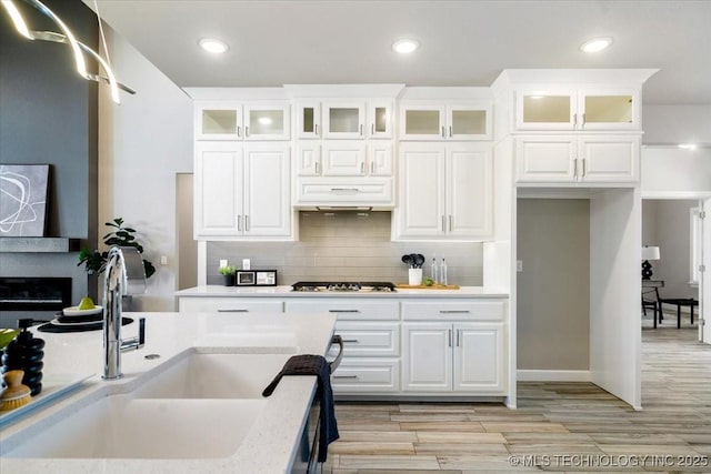 kitchen with stainless steel gas cooktop, a sink, light countertops, light wood-style floors, and backsplash