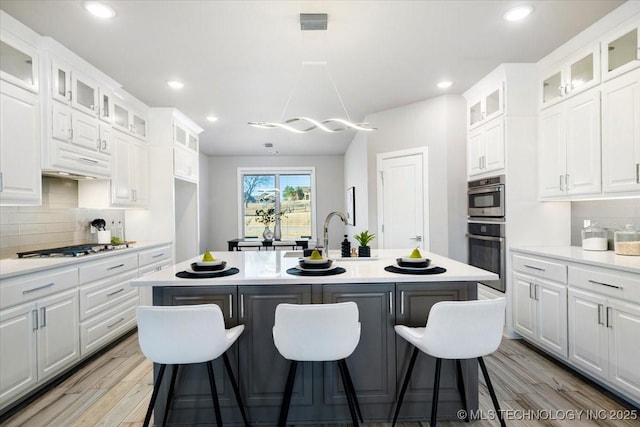 kitchen with gas cooktop, a breakfast bar area, an island with sink, light countertops, and light wood-style floors