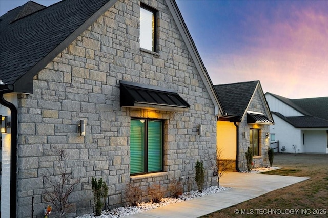 view of front of property featuring a standing seam roof, stone siding, roof with shingles, and metal roof