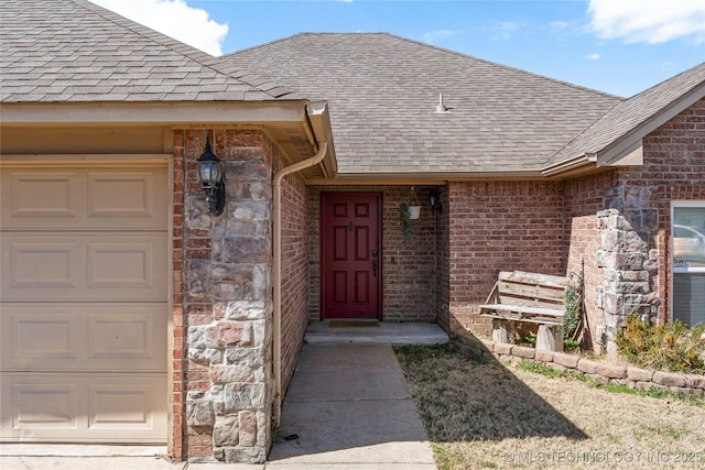 doorway to property with stone siding, brick siding, a garage, and roof with shingles