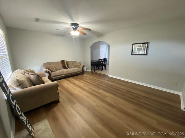 living room featuring visible vents, baseboards, wood finished floors, arched walkways, and a ceiling fan