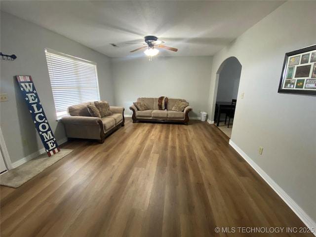 unfurnished living room featuring ceiling fan, baseboards, arched walkways, and wood finished floors