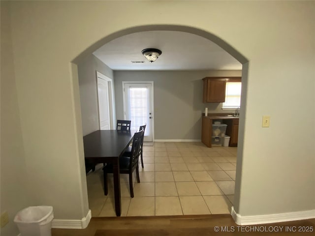 dining room with arched walkways, light tile patterned floors, a healthy amount of sunlight, and baseboards