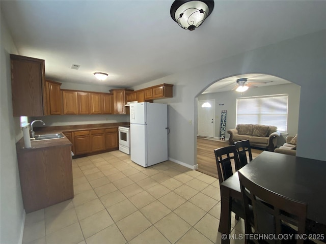 kitchen with white appliances, brown cabinetry, visible vents, arched walkways, and a sink