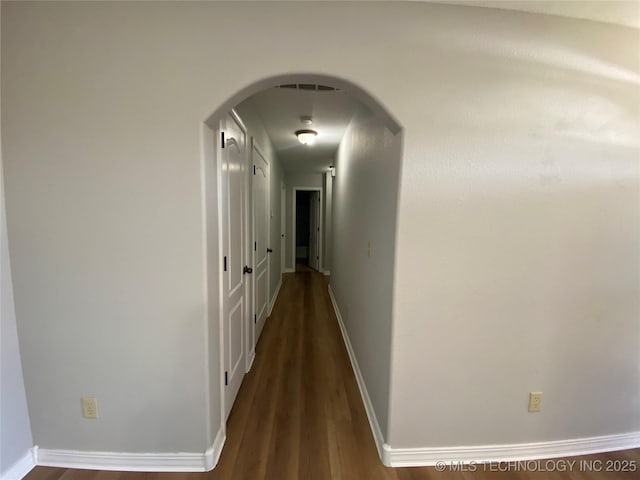 corridor featuring baseboards, arched walkways, and dark wood-style flooring