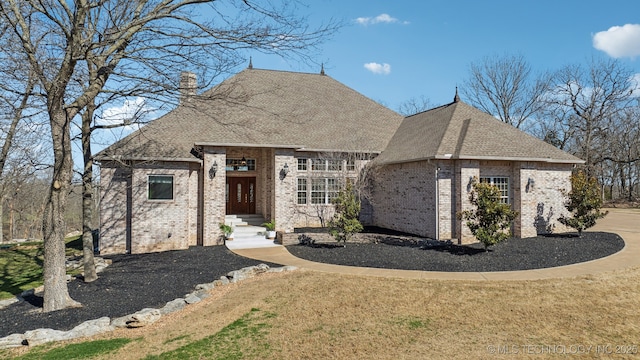 french country style house featuring a front lawn, brick siding, a chimney, and a shingled roof