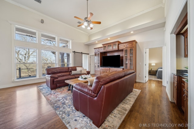 living room featuring dark wood-type flooring, baseboards, a barn door, ornamental molding, and a high ceiling