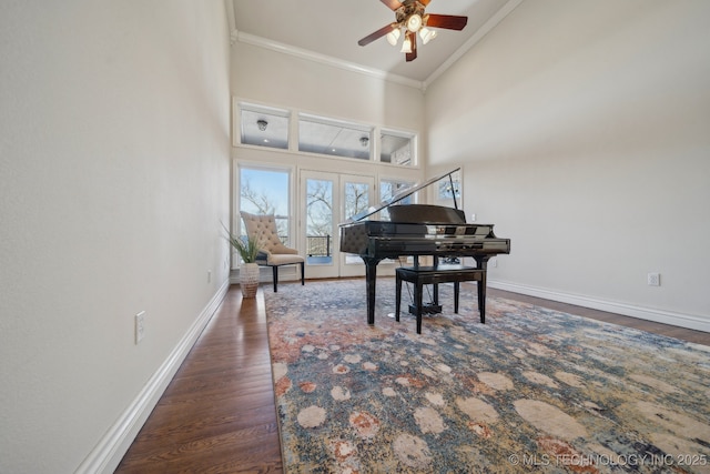 living area with a high ceiling, crown molding, baseboards, and wood finished floors