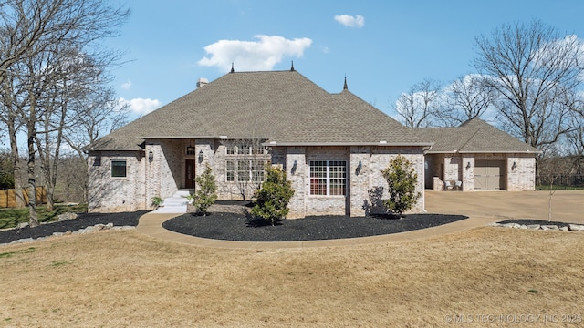 french country style house featuring a front yard, driveway, a shingled roof, a garage, and brick siding