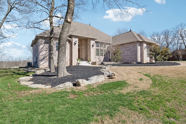 view of front of home featuring brick siding, a front lawn, and roof with shingles