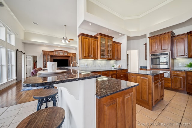 kitchen with a breakfast bar area, light tile patterned flooring, ornamental molding, a barn door, and open floor plan