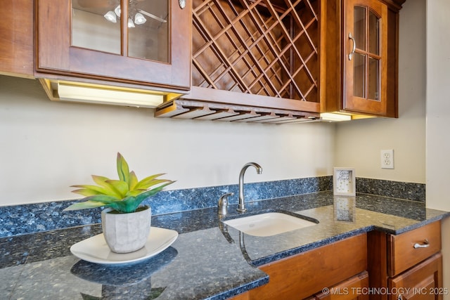 interior space featuring a sink, glass insert cabinets, brown cabinets, and dark stone countertops