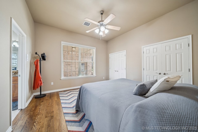 bedroom featuring wood finished floors, visible vents, baseboards, ceiling fan, and two closets