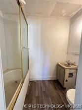 bathroom featuring toilet, wood finished floors, baseboards, and shower / washtub combination