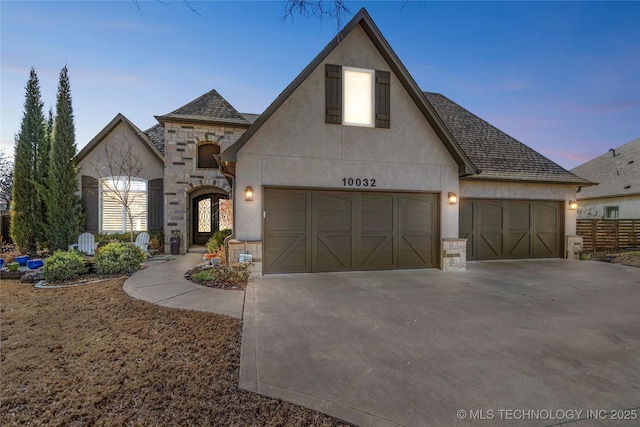 french provincial home with fence, stucco siding, a garage, stone siding, and driveway