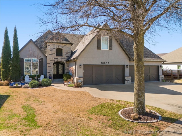 french country home featuring stucco siding, stone siding, fence, french doors, and an attached garage