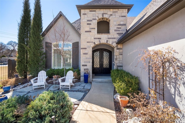 view of exterior entry featuring stone siding, stucco siding, french doors, and fence