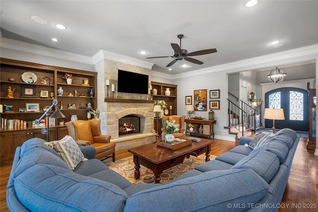 living area with wood finished floors, stairs, a stone fireplace, french doors, and crown molding