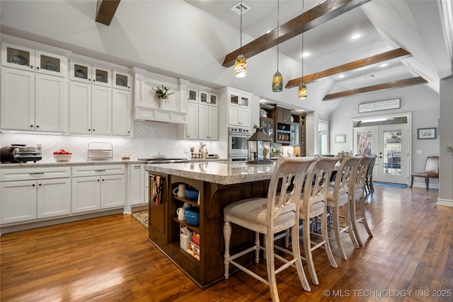 kitchen with a breakfast bar area, wood finished floors, beam ceiling, decorative backsplash, and french doors