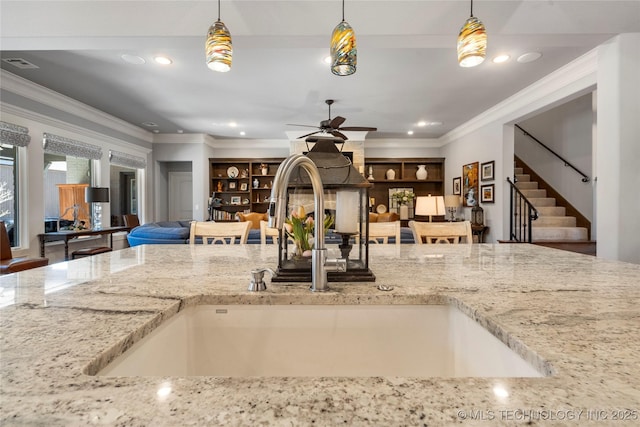 kitchen with visible vents, pendant lighting, ornamental molding, a sink, and light stone counters