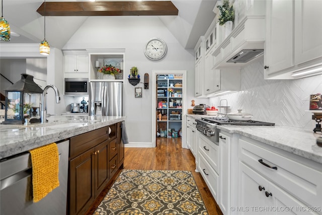 kitchen with a sink, appliances with stainless steel finishes, white cabinets, and vaulted ceiling with beams