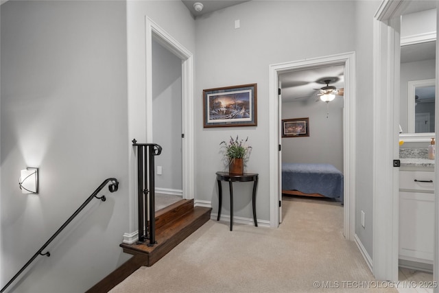 hall with an upstairs landing, light carpet, and baseboards